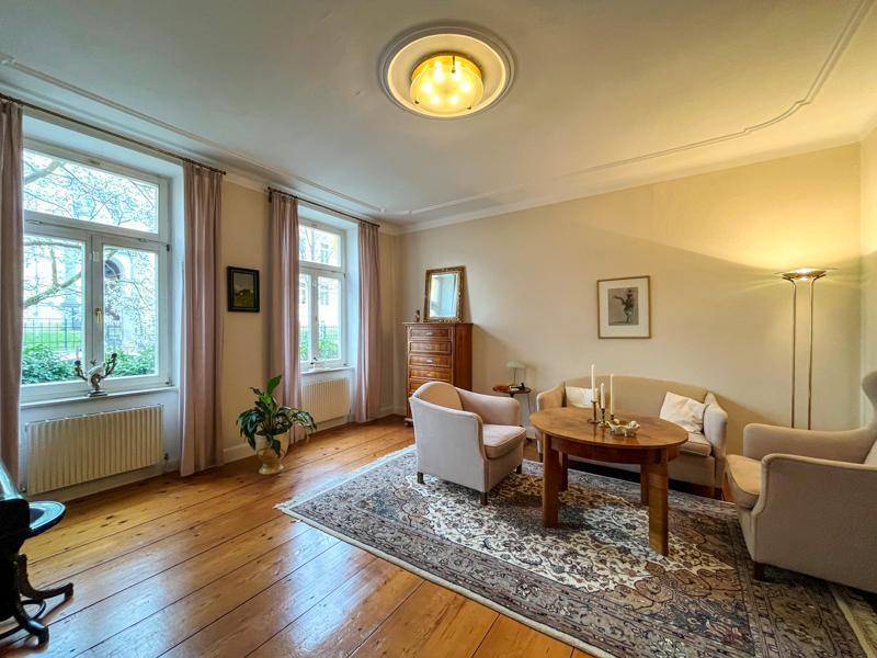 Elegantes Wohnzimmer mit Holzdielenboden, beigem Teppich und hohen Fenstern, die viel Tageslicht hereinlassen.