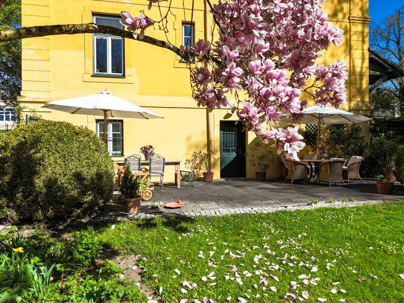 Gemütliche Terrasse mit Gartenmöbeln und Sonnenschirmen, angrenzend an einen blühenden Garten mit Magnolienbaum.