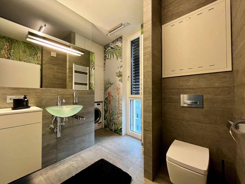 Modernes Badezimmer mit Wand-WC, grünem Waschbecken und floraler Tapete.
