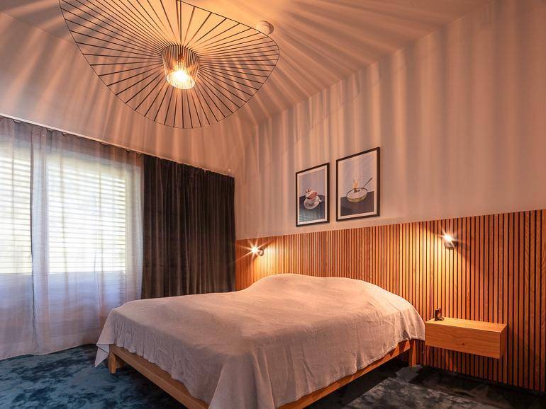 Gemütliches Schlafzimmer mit Holzbett, auffälliger Deckenleuchte und weichem Teppichboden.