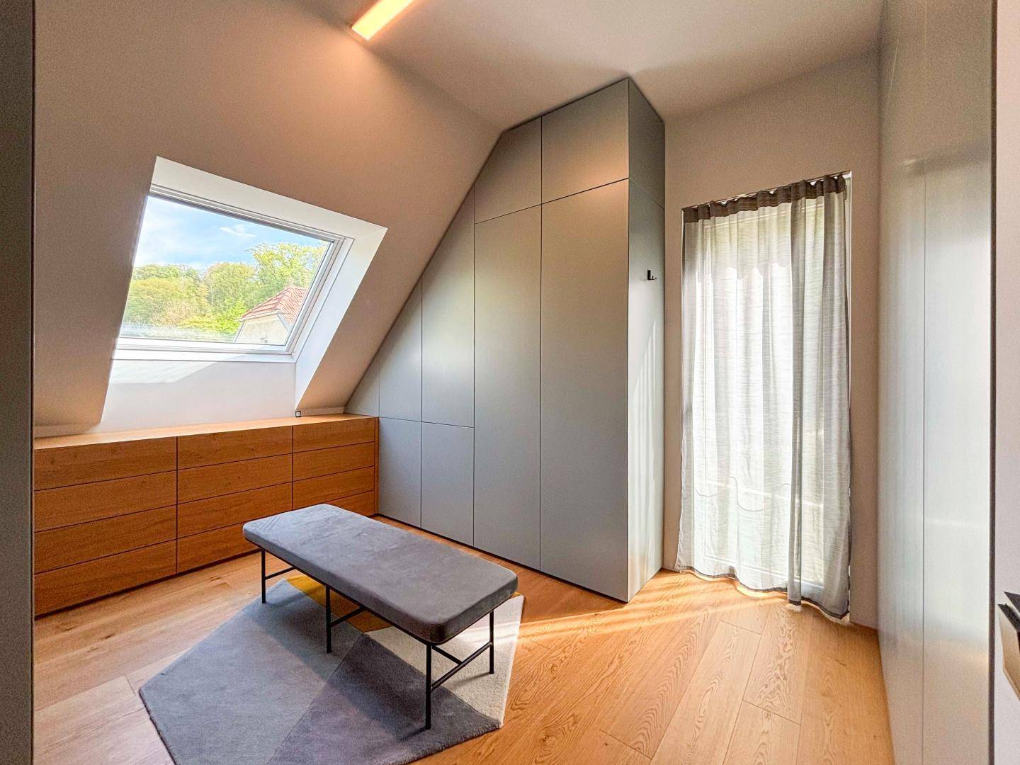 Schlafzimmer mit Einbauschränken, Holzkommode und großem Dachfenster für viel Licht.