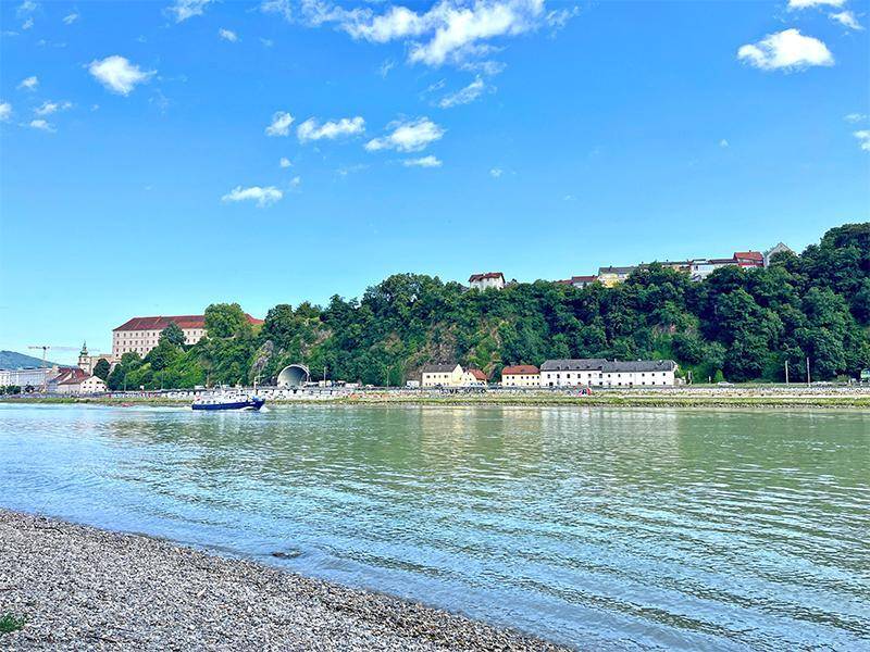 Malerischer Blick auf den breiten Fluss, die historische Bebauung und die grünen Uferlandschaften.