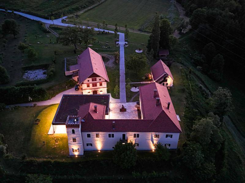 Nächtliche Luftaufnahme des gesamten Anwesens mit beleuchteten Gebäuden und der umliegenden dunklen Landschaft.