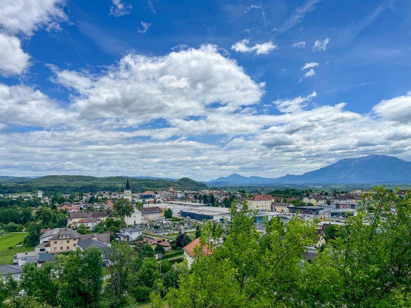 Weitläufiger Panoramablick über eine Stadt und die umliegende Landschaft mit Bergen unter bewölktem Himmel.