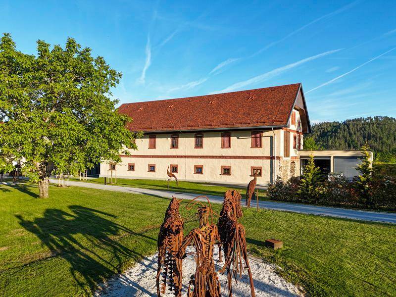 Großes traditionelles Gebäude mit rotem Dach, umgeben von Rasen und Bäumen, mit mehreren Skulpturen.
