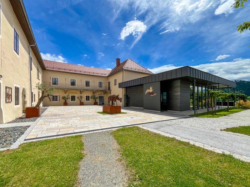 Weitläufiger Innenhof mit moderner Gebäudeerweiterung, gepflastertem Bereich und Skulptur unter blauem Himmel.
