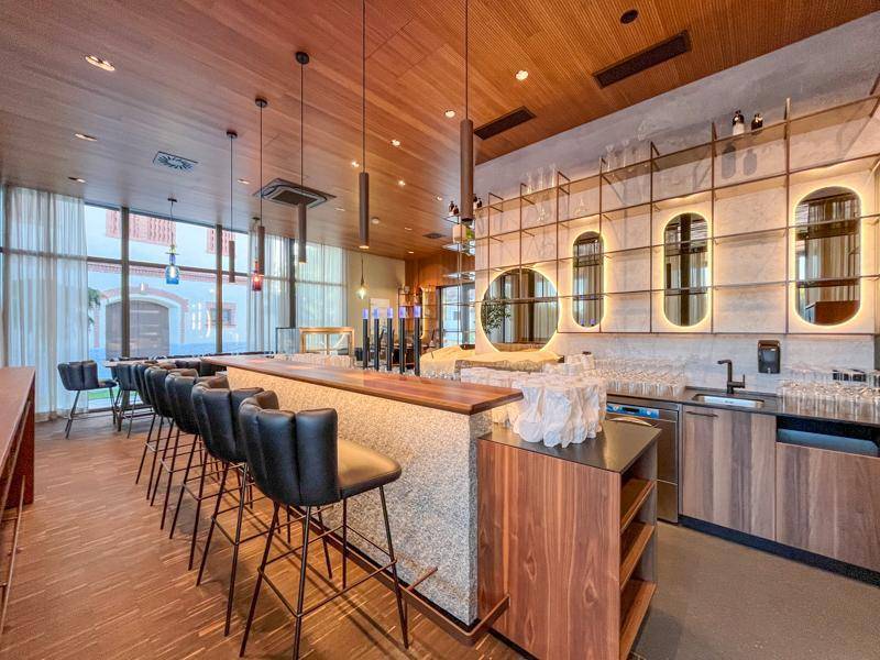 Elegante moderne Bar mit Holzdecke, Steintheke, Barhockern und beleuchteten Spiegelregalen.
