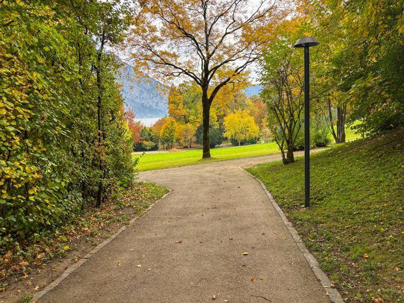 Herbstliche Parklandschaft mit Spazierweg, bunten Bäumen und Blick auf den See.