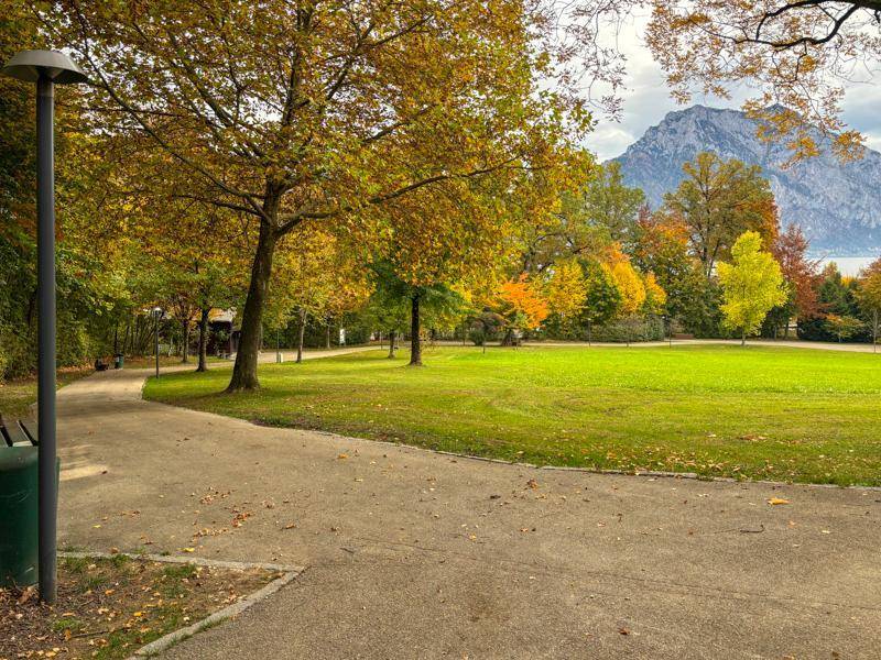 Weitläufige Parkanlage im Herbst mit grünen Wiesen und Bergblick.