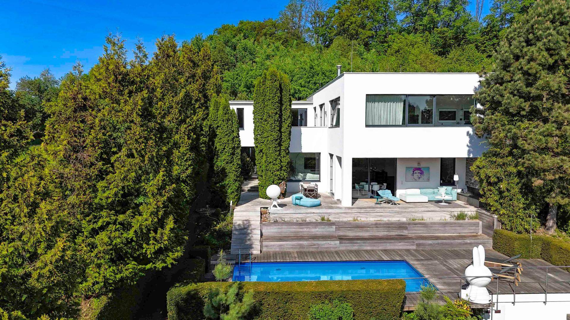 Moderne Villa mit weitläufiger Holzterrasse, Swimmingpool und üppiger grüner Umgebung.