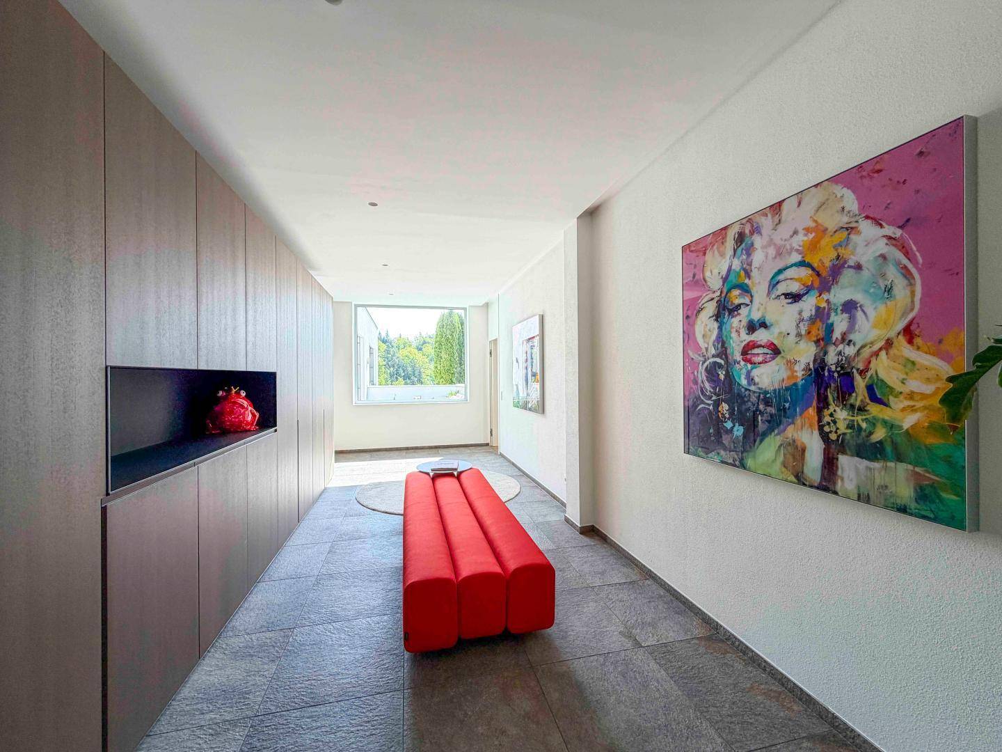 Heller Flur mit modernen Einbauschränken, Kunstwerken und großformatigen Bodenfliesen.