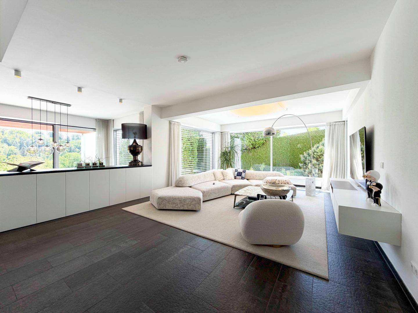 Elegantes Wohnzimmer mit dunklem Holzboden, großen Fenstern und Blick in den Garten.