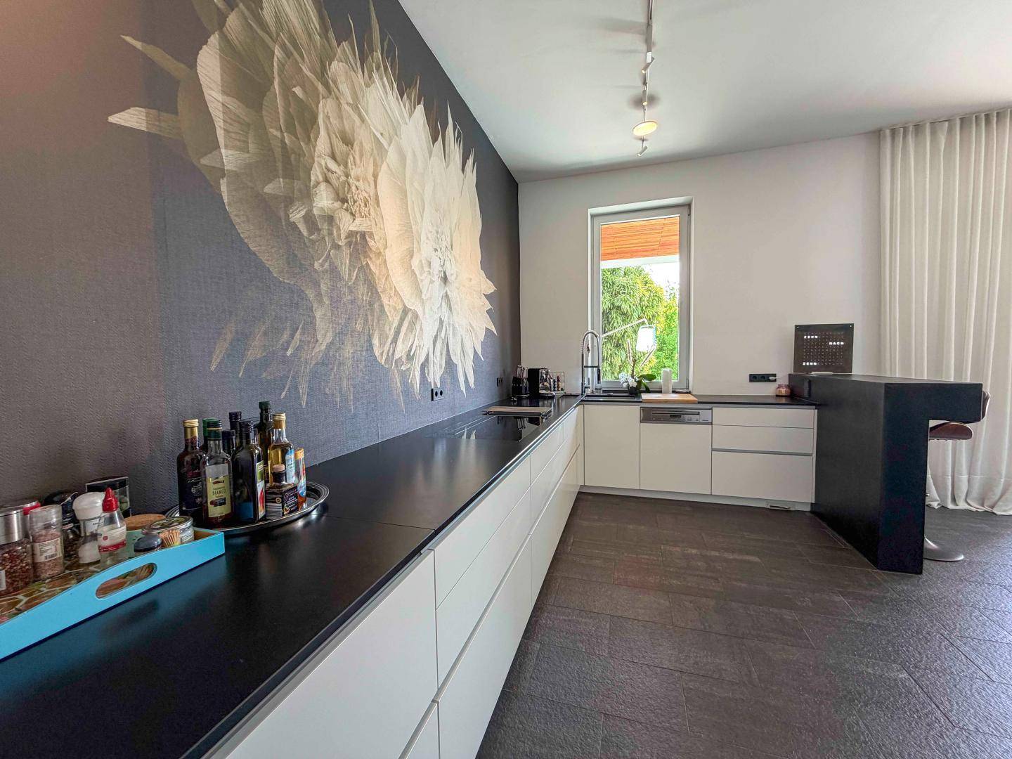 Moderne Küche mit weißen Unterschränken, dunkler Arbeitsplatte und großem Blumenwandbild.