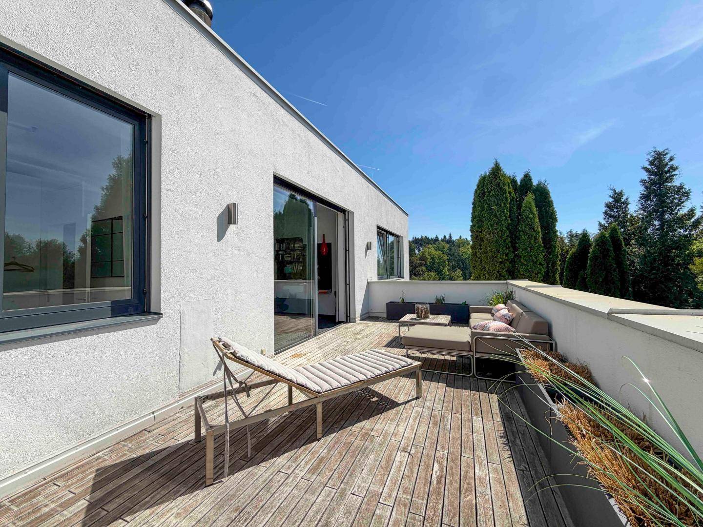 Sonniger Dachterrasse mit Holzdeck, Liegestuhl und weitem Blick in die Natur.