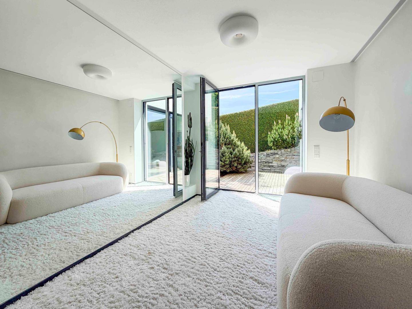 Helles Wohnzimmer mit flauschigem Teppich, Spiegelfront und Zugang zum Außenbereich.