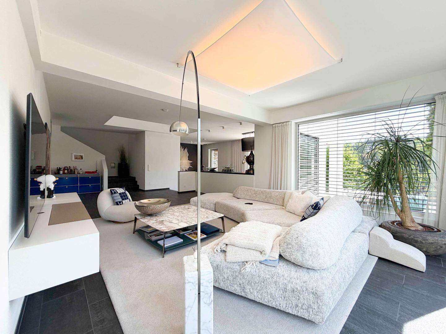 Modernes Wohnzimmer mit großzügiger Sofalandschaft, Marmortisch und Blick ins Grüne.