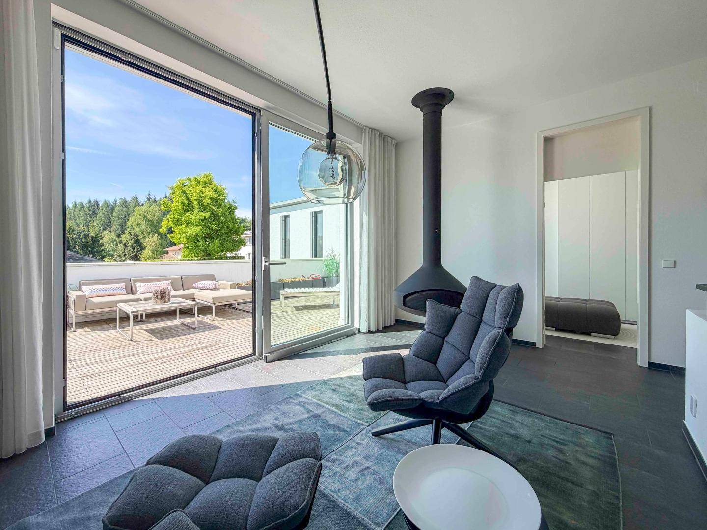 Gemütliches Wohnzimmer mit modernem Hängekamin, bequemen Sesseln und Terrassenzugang.