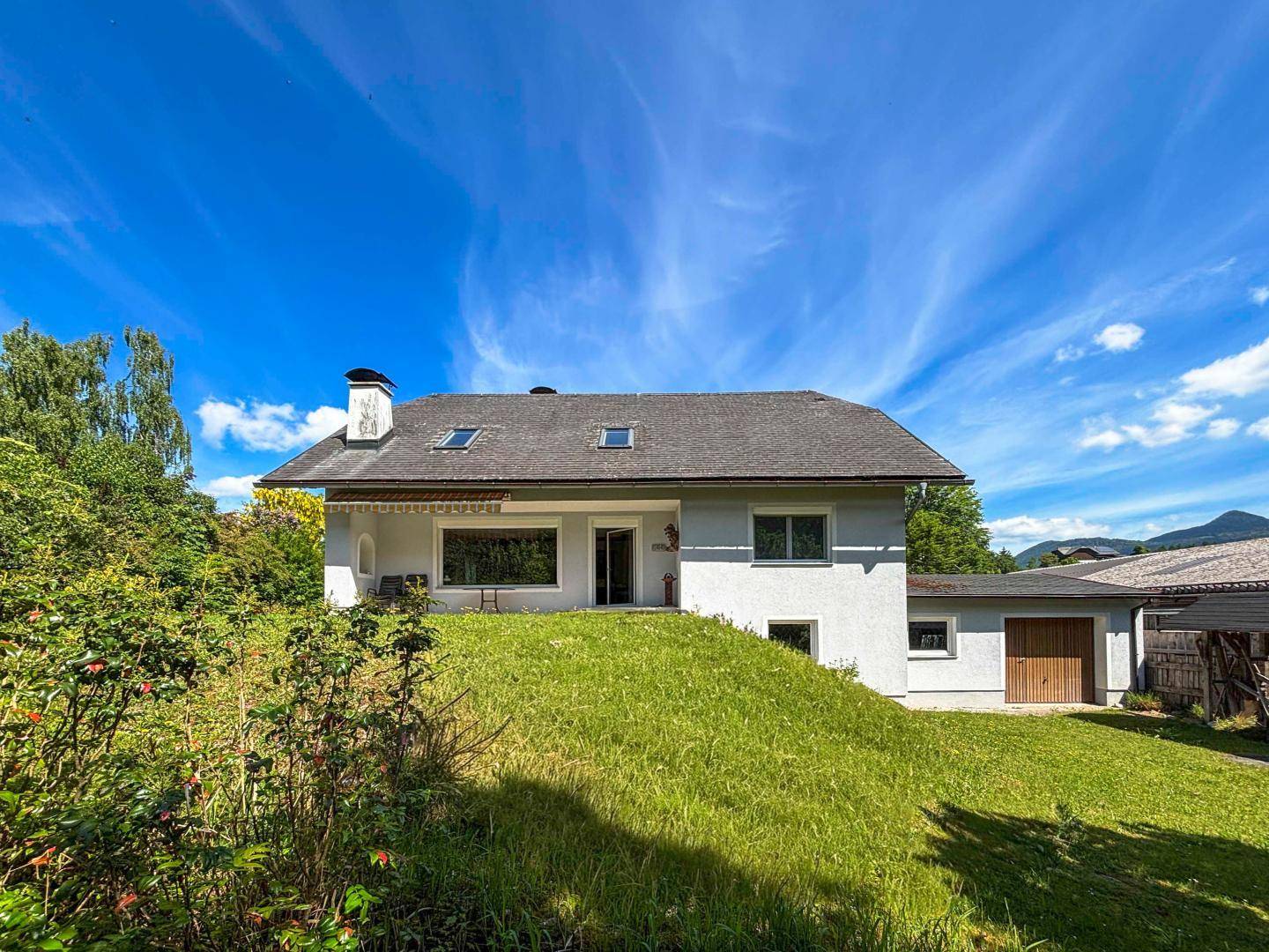 Freistehendes Haus mit weißer Fassade, Satteldach und Garage, umgeben von Grünflächen.