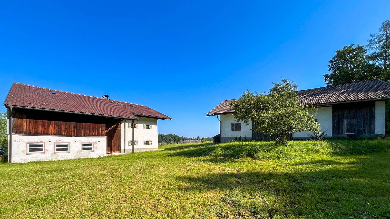 Zwei traditionelle Gebäude auf einem weitläufigen Grundstück mit grünen Wiesen und Bäumen unter blauem Himmel.