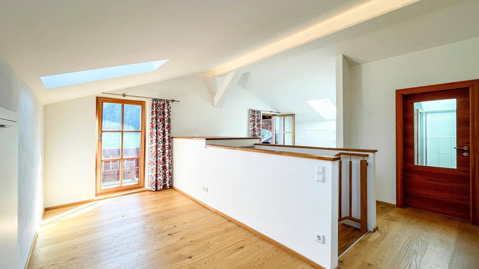 Heller Flurbereich im Obergeschoss mit Holzboden, Dachfenstern und Zugang zu einem weiteren Balkon.