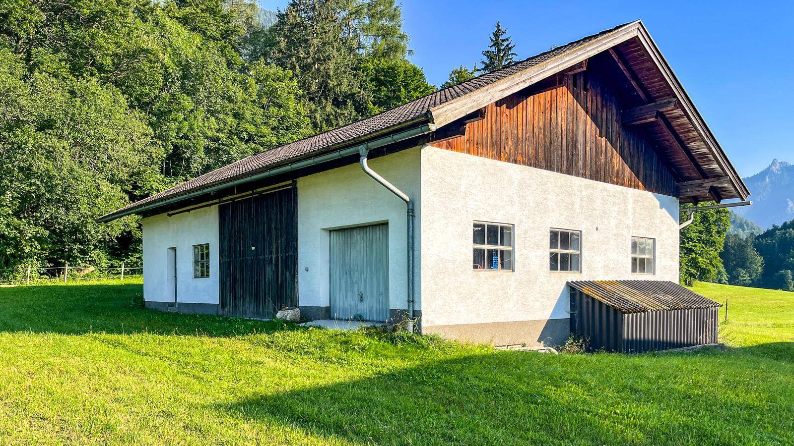 Traditionelles Nebengebäude mit weißer Fassade und Holzelementen, umgeben von grünen Wiesen und Bäumen.