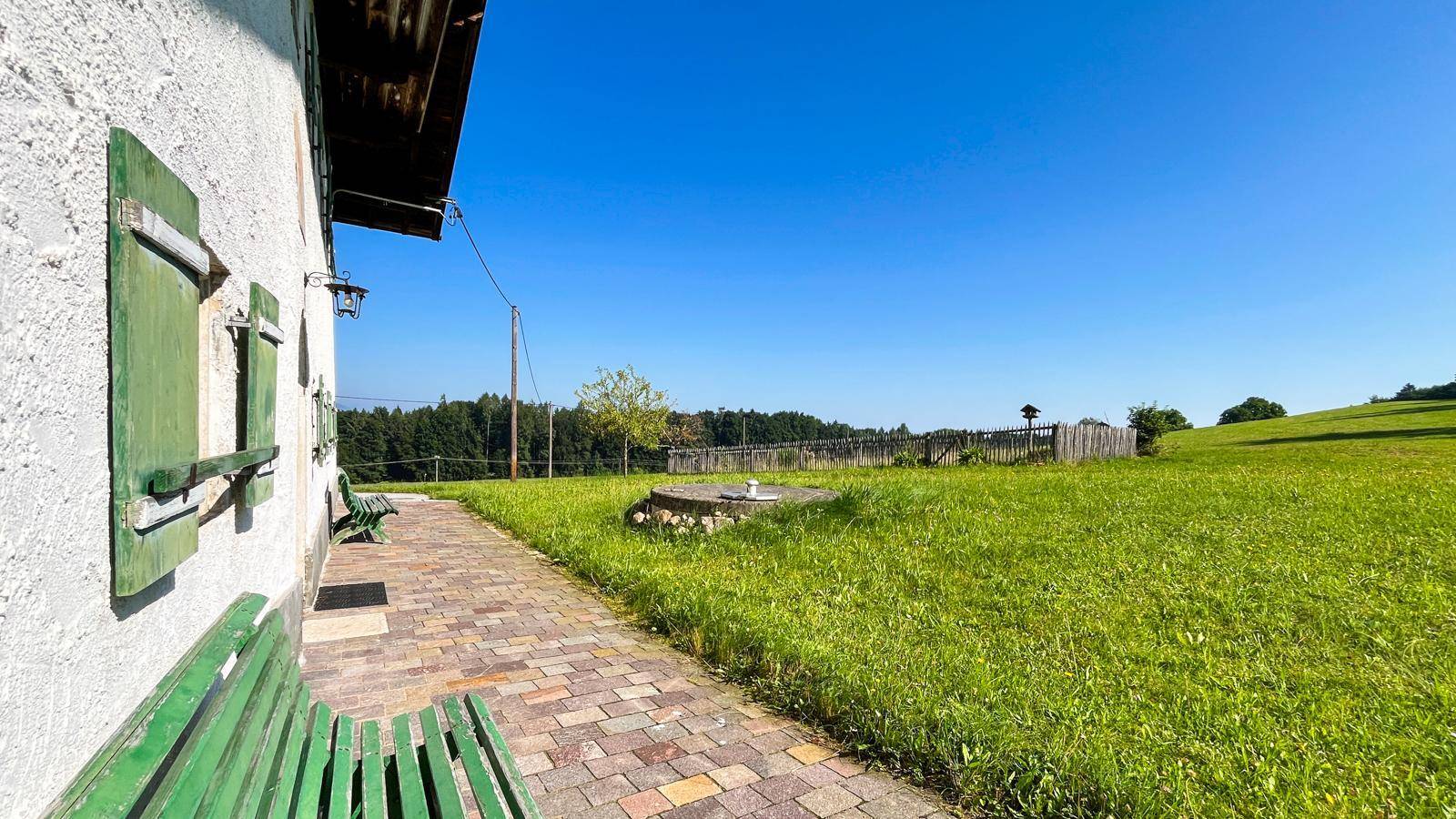 Gepflasterter Weg entlang des Hauses mit grünen Bänken und einem kleinen umzäunten Gartenbereich.