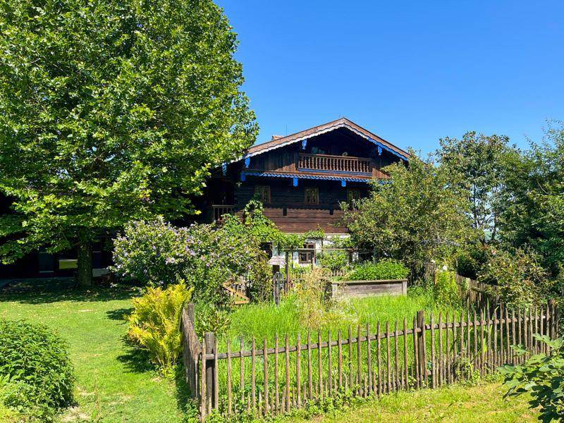 Idyllischer Garten mit Holzzaun und Blick auf das traditionelle Haus mit Balkon.
