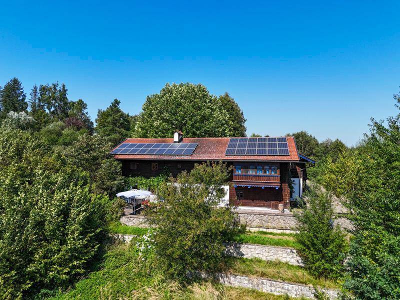Traditionelles Haus mit Ziegeldach und Photovoltaikanlage, umgeben von üppiger grüner Natur.