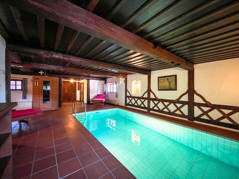 Innenpoolbereich mit Terrakotta-Fliesenboden, Holzbalken und einer sichtbaren Sauna.