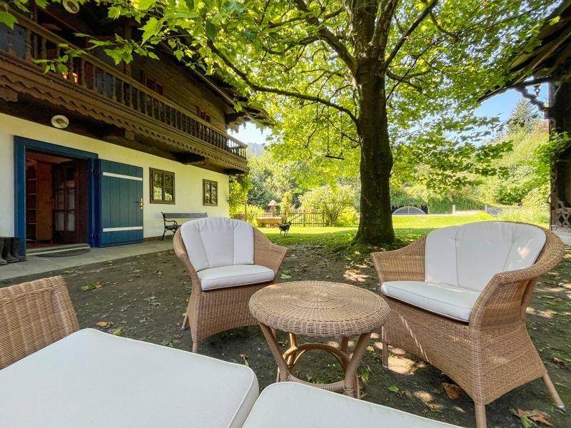 Entspannter Sitzbereich im Garten mit Korbmöbeln, umgeben von grüner Natur und traditionellen Häusern.