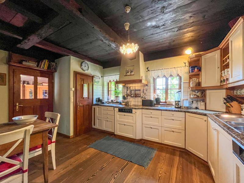 Rustikale Küche mit Holzboden, weißen Einbauschränken und dunklen Deckenbalken.