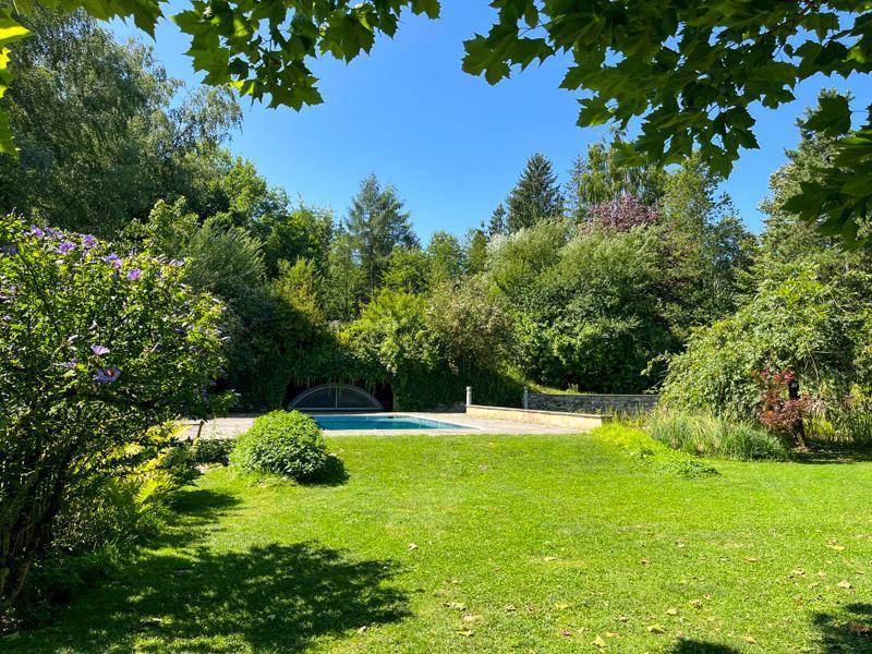 Weitläufiger Rasenbereich mit üppiger Vegetation und einem versteckten Pool im Hintergrund.