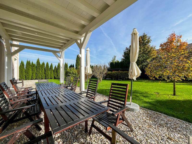 Überdachte Terrasse mit großem Holztisch und Stühlen, ideal für Mahlzeiten im Freien.