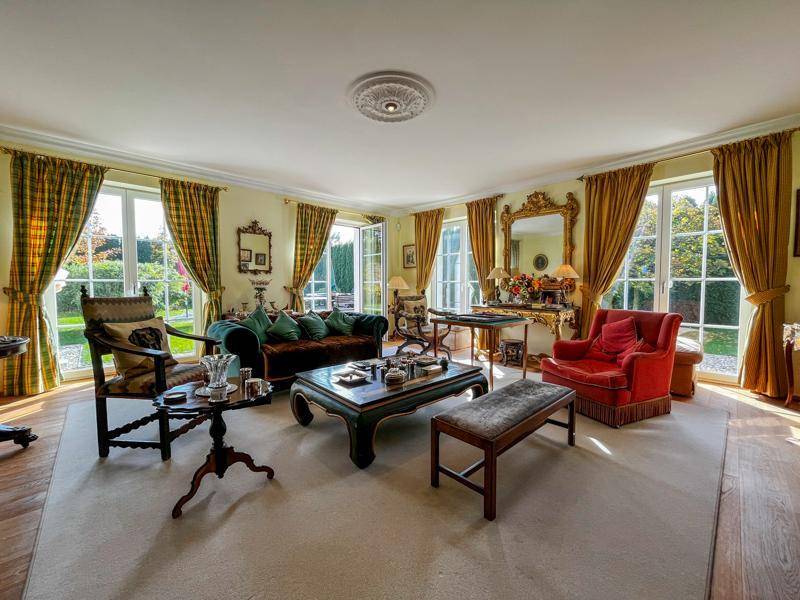 Elegantes Wohnzimmer mit großen Fenstern, klassischer Einrichtung und Zugang zum Garten.