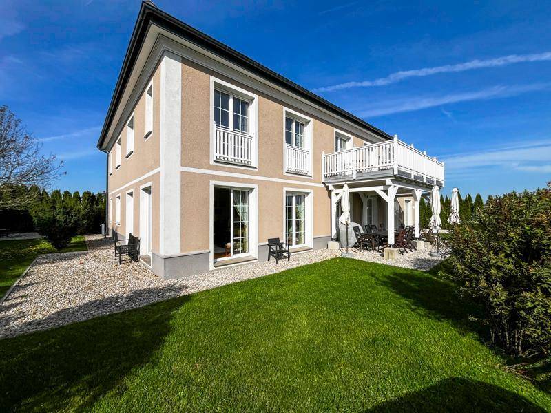 Elegantes Landhaus mit beiger Fassade, weißen Balkonen und gepflegtem Gartenbereich.