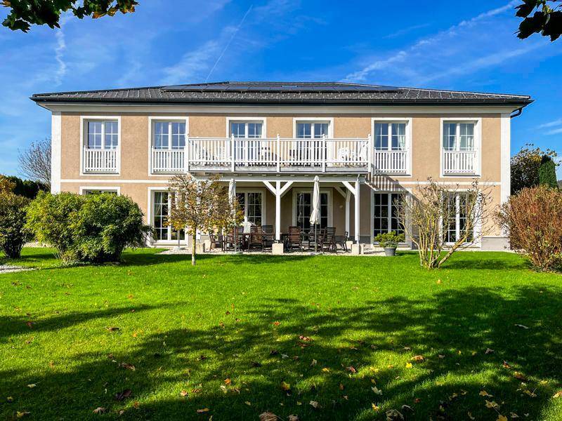 Vorderansicht eines stilvollen Landhauses mit großem Rasen und sonnigen Terrassenbereichen.