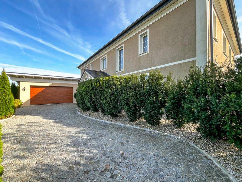 Gepflasterte Auffahrt mit Garage und gepflegten Hecken, die zum Haus führt.