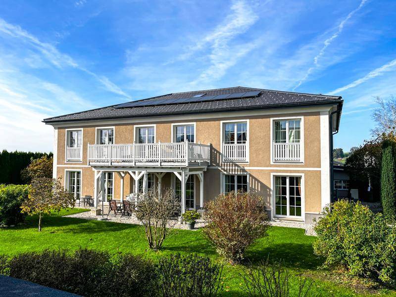 Charmantes Landhaus mit beiger Fassade, weißen Balkonen und weitläufigem, grünem Garten.