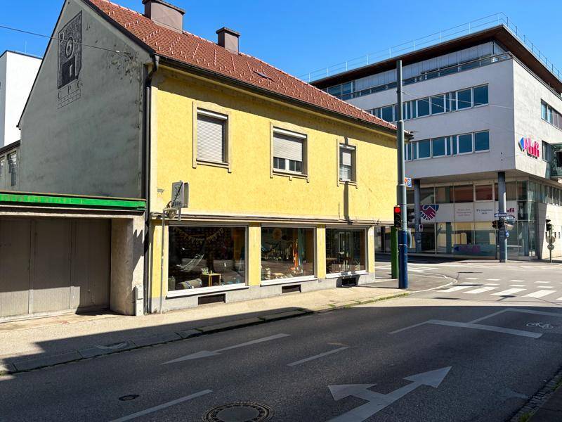 Vorderansicht des gelben Gebäudes mit großen Schaufenstern und angrenzender moderner Bebauung.