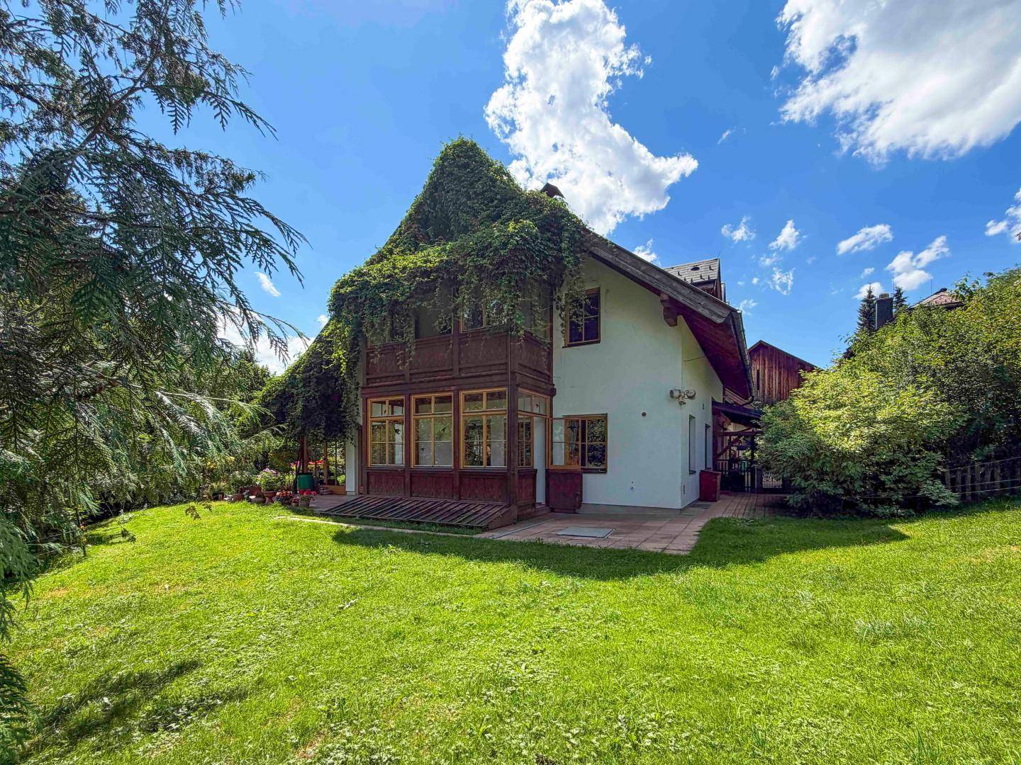 Charmantes Haus mit bewachsenem Dach und Holzdetails, eingebettet in einen weitläufigen grünen Garten.