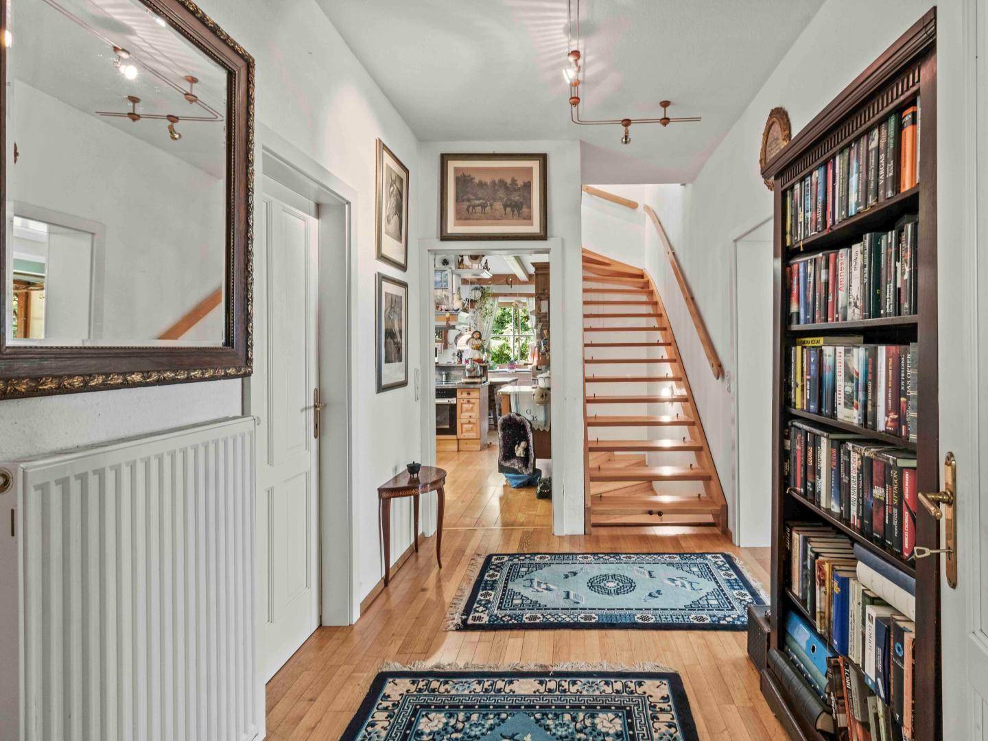 Geräumiger Flur mit Holztreppe, Parkettboden und einem Bücherregal, das zum Wohnbereich führt.