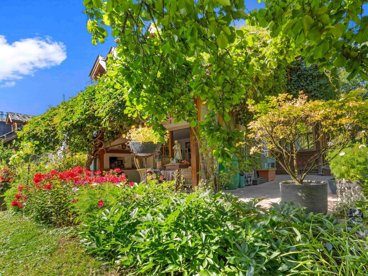 Üppiger Gartenbereich mit blühenden Pflanzen und einer Terrasse, umgeben von reicher Vegetation.