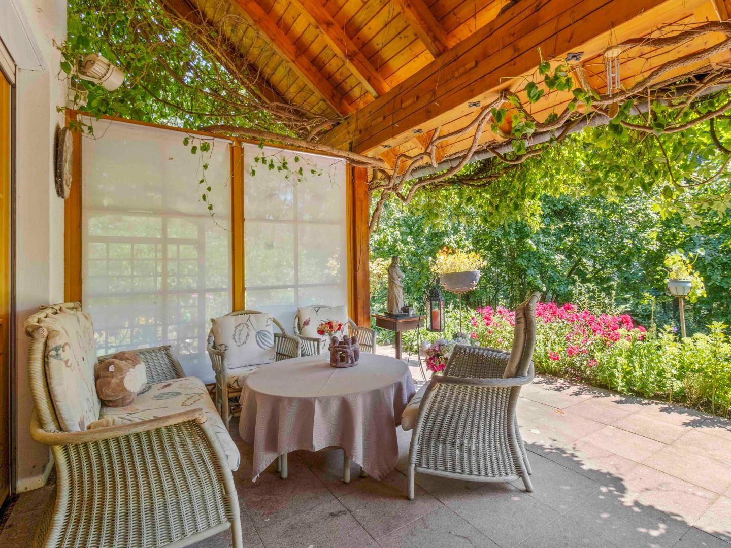 Schattige Terrasse mit Korbmöbeln und Blick in den blühenden Garten, ideal zum Entspannen.