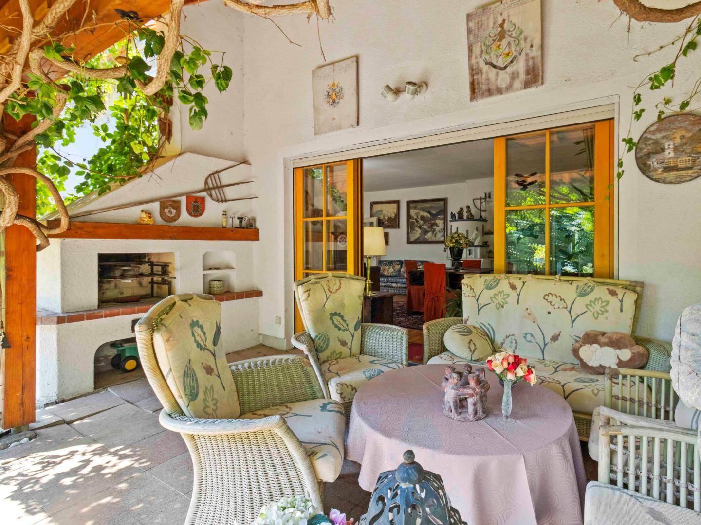 Gemütliche überdachte Terrasse mit Korbmöbeln und integriertem Grill, ideal für entspannte Stunden.