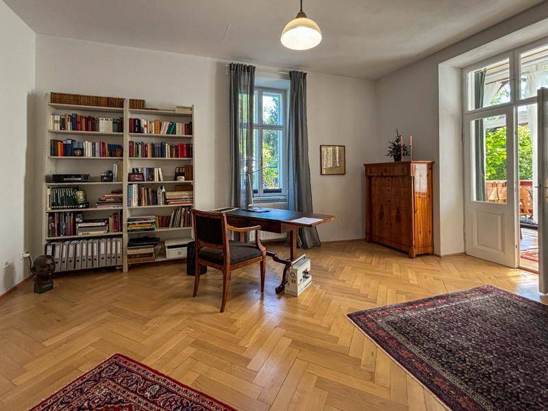 Helles Arbeitszimmer mit Fischgrätparkett, großem Bücherregal und Zugang zum Balkon.