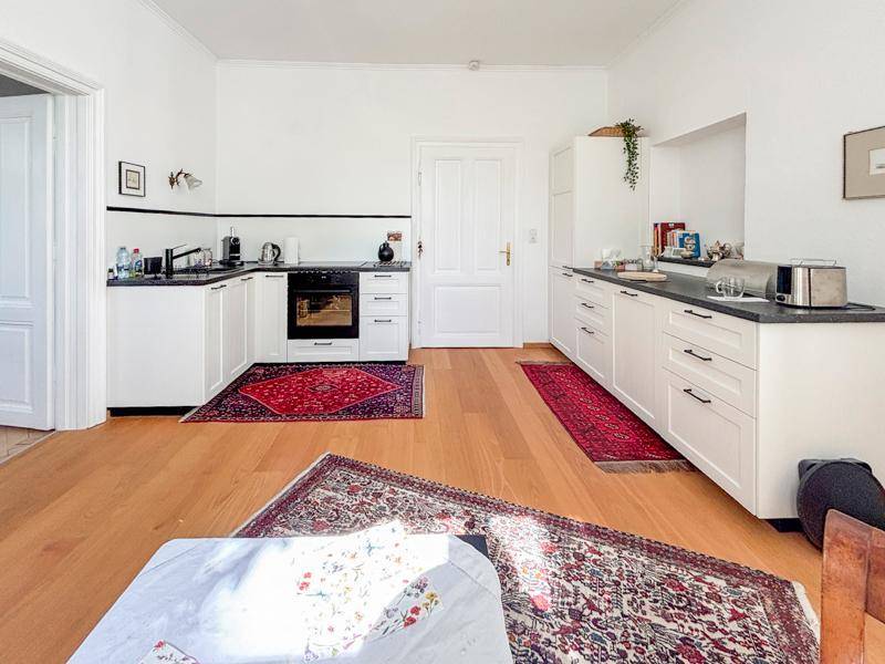 Helle Küche mit weißen Schränken, dunkler Arbeitsplatte und Holzboden.