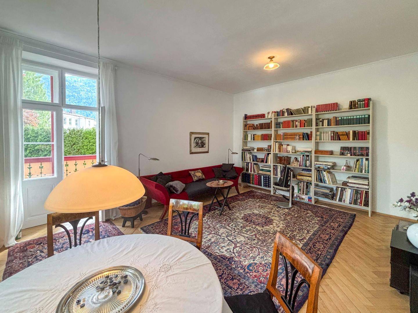 Geräumiger Wohn- und Essbereich mit Bücherregal, Sofa und Blick ins Grüne.
