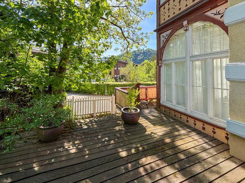Sonnige Holzterrasse mit Blick ins Grüne und traditioneller Fassadenverzierung.