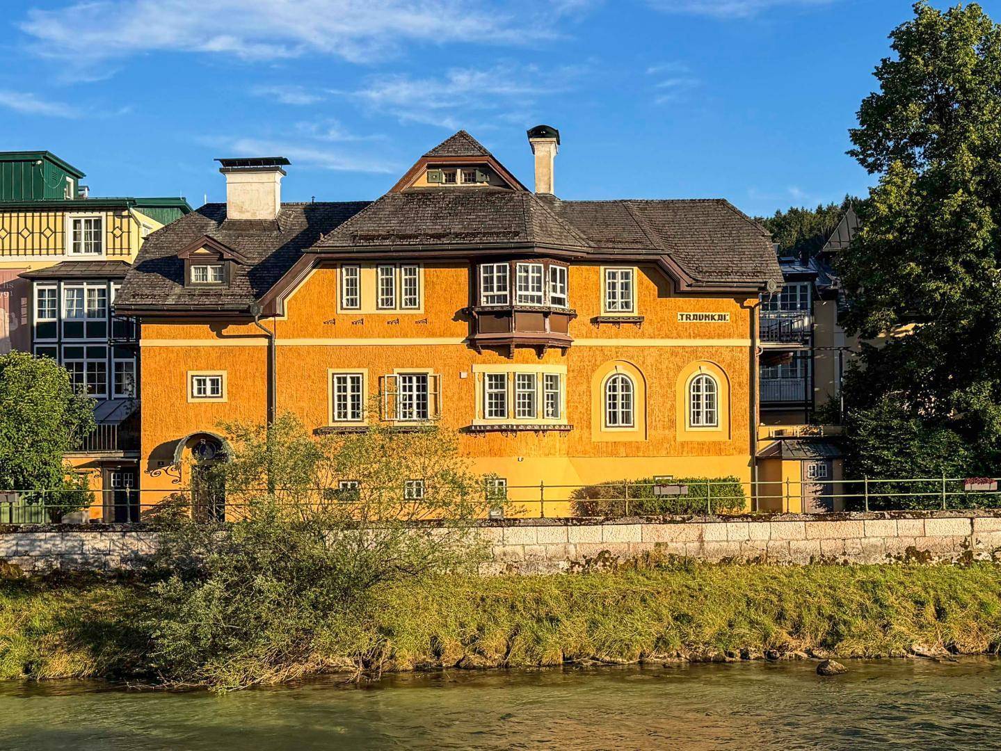 Historisches gelbes Gebäude am Flussufer mit Bergblick und traditioneller Architektur.