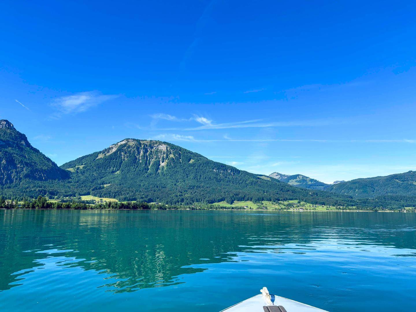 Weitblick über einen ruhigen See mit bewaldeten Bergen unter klarem blauem Himmel.